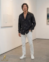 Man wearing a black patterned shirt and white pants in an art gallery setting