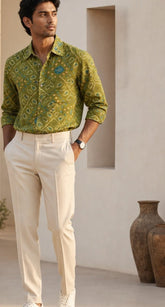 Man wearing a green patterned shirt and beige pants in a minimalistic room.