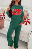 Person wearing a green 'MERRY' sweater in a cozy living room setting.