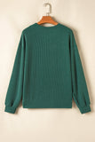 Green ribbed sweater on a wooden hanger against a beige background