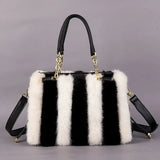 Black and white striped handbag with fur trim on a gray background
