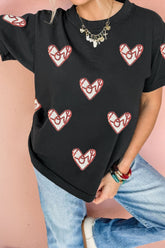 Person wearing a black t-shirt with red heart designs on a pink background