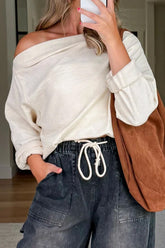 Person wearing a white off-shoulder top and dark jeans, holding a brown bag.