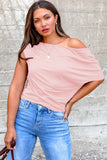 Woman wearing a pink off-shoulder top and blue jeans against a gray wall.