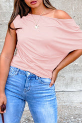 Person wearing a pink off-shoulder top and blue jeans against a gray concrete wall.