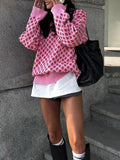 Person wearing a pink patterned sweater, white skirt, and black boots against a gray wall.