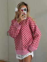Person wearing a pink sweater with a red pattern, taking a mirror selfie.