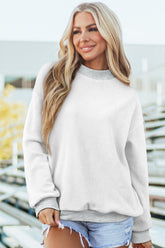 Woman wearing a light gray sweatshirt and denim shorts with a blurred outdoor background