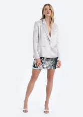 Woman wearing a white blazer and silver sequin skirt on a white background