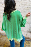 Person wearing a green sweater with a textured pattern against a stone wall background