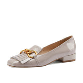 Beige patent leather shoe with gold chain detail on a white background