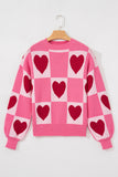 Pink heart checkered crew neck sweater with ribbed cuffs on a hanger, front view
