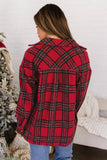 A woman shown from the back wearing a red plaid flannel shirt with black and green stripes, paired with blue jeans, standing in a cozy indoor setting with a white brick wall, a Christmas tree, and a white knit blanket.