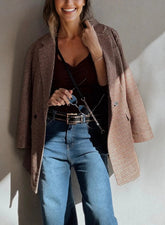 Woman wearing a plaid coat, black top, and blue jeans against a neutral wall.