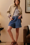 Woman wearing a beige jacket, striped shirt, and blue shorts indoors.