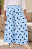 Person wearing light blue wide-leg polka-dot pants, white long-sleeve top, and beige sneakers indoors.