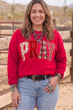 Smiling woman in red “PRAY” western sweatshirt with light blue jeans and turquoise jewelry.