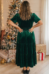 Back view of woman in dark green velvet tiered midi dress with puff sleeve.