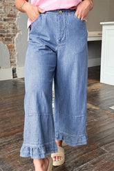 Woman in pink top, light blue ruffle-hem wide jeans, beige espadrille sandals.