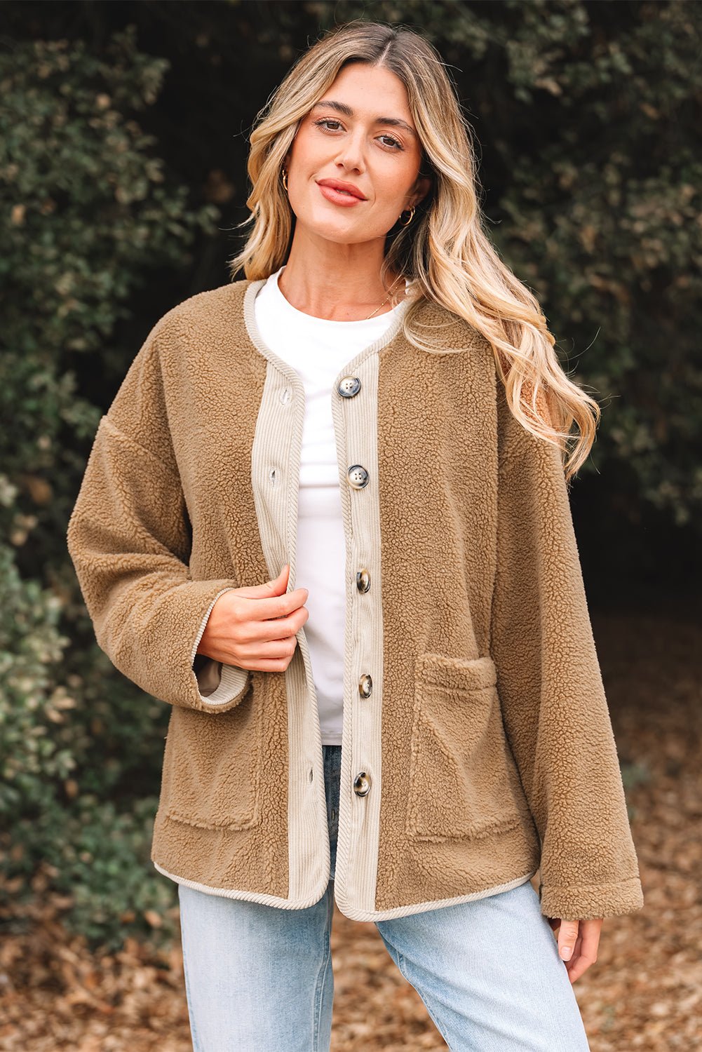 Woman wearing a brown cardigan with a white shirt and light blue jeans, standing outdoors.