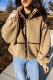 Woman in tan sherpa fleece jacket with black trim and light blue jeans.
