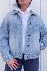 Person wearing light blue polka-dot denim jacket over white hoodie and navy pants against paneled wall.