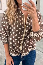 Woman in brown and beige polka dot zip-up jacket with ruffled trim and blue jeans, mirror selfie.