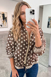 A woman takes a mirror selfie wearing a brown and white polka dot zip-up bomber jacket