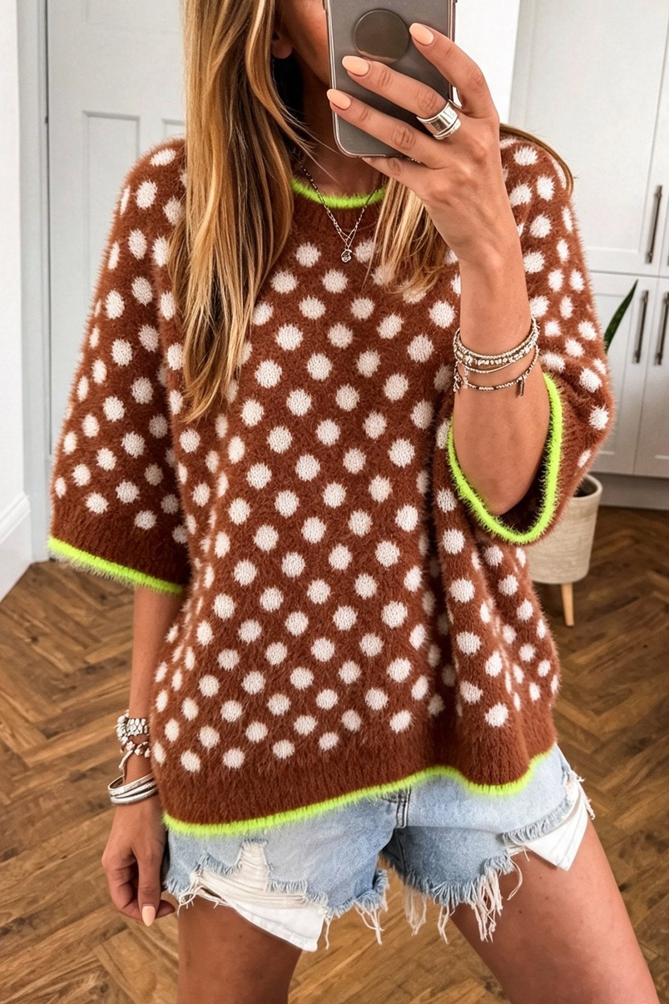 Woman in brown fuzzy polka-dot sweater with neon green trim and denim shorts.