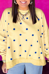Woman in pale yellow crewneck sweatshirt with blue polka dots and blue/white striped pants on pink background.