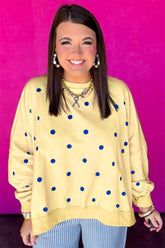 Smiling woman in pale yellow blue-dot sweatshirt & striped pants on pink wall.