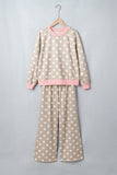 Beige polka-dot pajama set with pink trim, hanging on a wooden hanger.