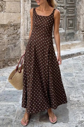 Woman wearing a brown polka dot dress standing on a stone street.