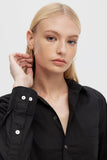 Woman wearing a black shirt with a button detail on a plain background