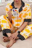 Person in pumpkin-print pajamas with polka-dot trim, holding a Halloween mug.