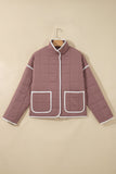 Dusty mauve quilted jacket with white piping trim hanging on a wooden hanger, beige background.