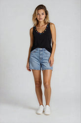 Woman wearing a black tank top with embellishments and denim shorts on a white background