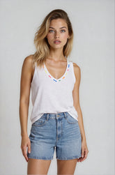 Woman wearing a white tank top with colorful accents and denim shorts on a plain background