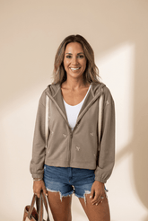 Woman wearing a beige hoodie with star patterns, white shirt, and denim shorts against a beige background