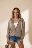 Woman wearing a beige hoodie with star patterns, white shirt, and denim shorts against a beige background