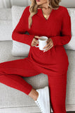 Woman in red ribbed V-neck lounge set sitting on sofa with white mug.