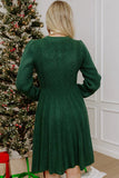 Back view of woman in dark green cable-knit long-sleeve dress by Christmas tree.