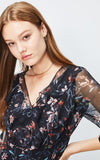 Woman wearing a floral dress with sheer sleeves on a light gray background