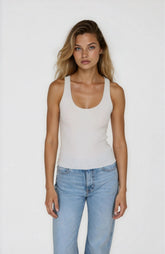 Woman wearing a white tank top and light blue jeans against a plain background