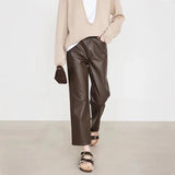 Person wearing a beige sweater and brown leather pants on a plain background