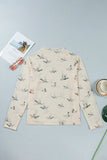 Cream mock-neck top with flying duck print, styled with glasses and magazine.
