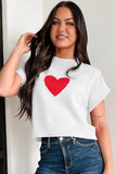 Woman wearing a white sweater with a red heart design against a plain background