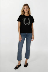 Woman wearing a black t-shirt with a horseshoe design and blue jeans on a white background