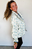 Side view of sky blue floral quilted puffer jacket with ruffle cuffs and black pants