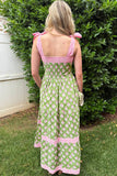 Woman wearing a green and pink dress with floral pattern standing in front of a bush.